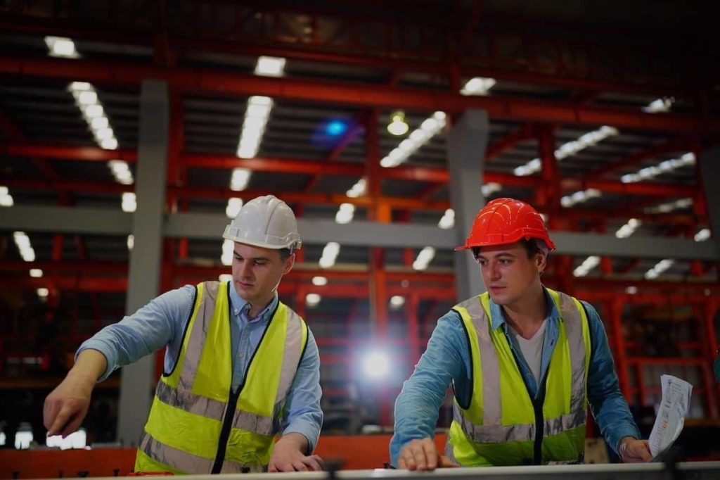 Factory workers in a factory wearing hard hats and safety vests.