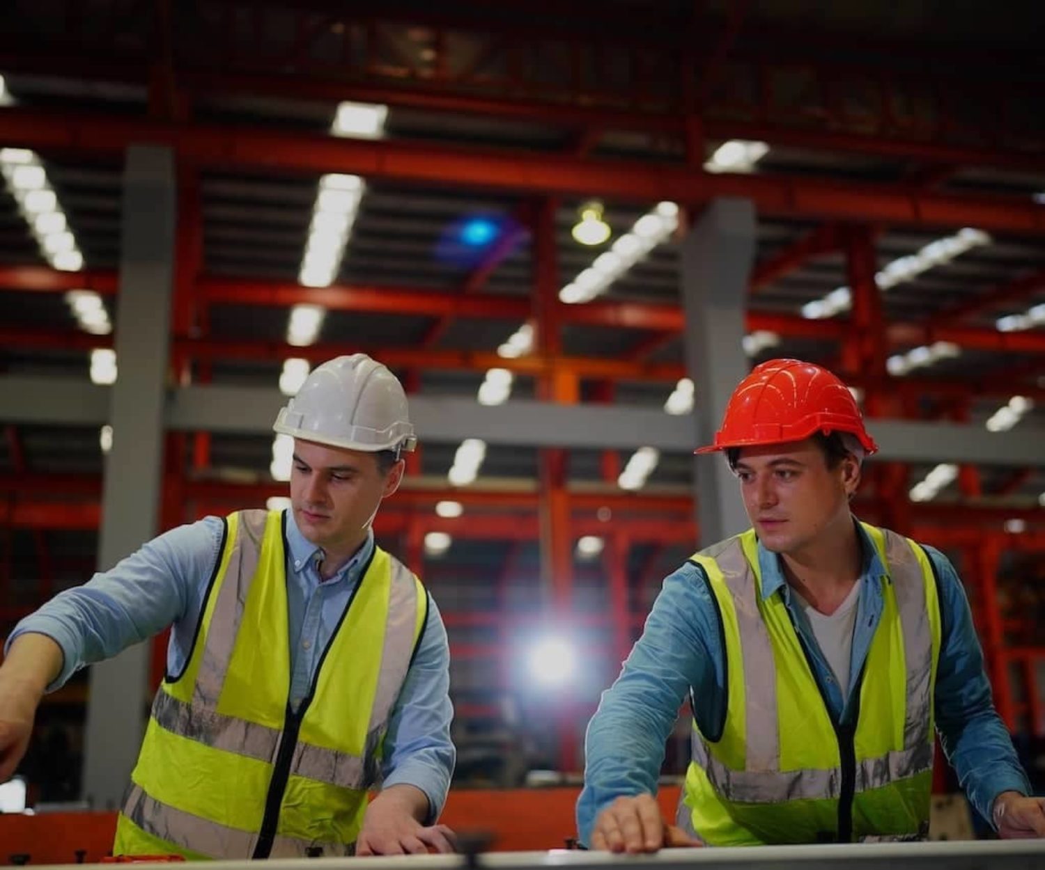 Factory workers in a factory wearing hard hats and safety vests.